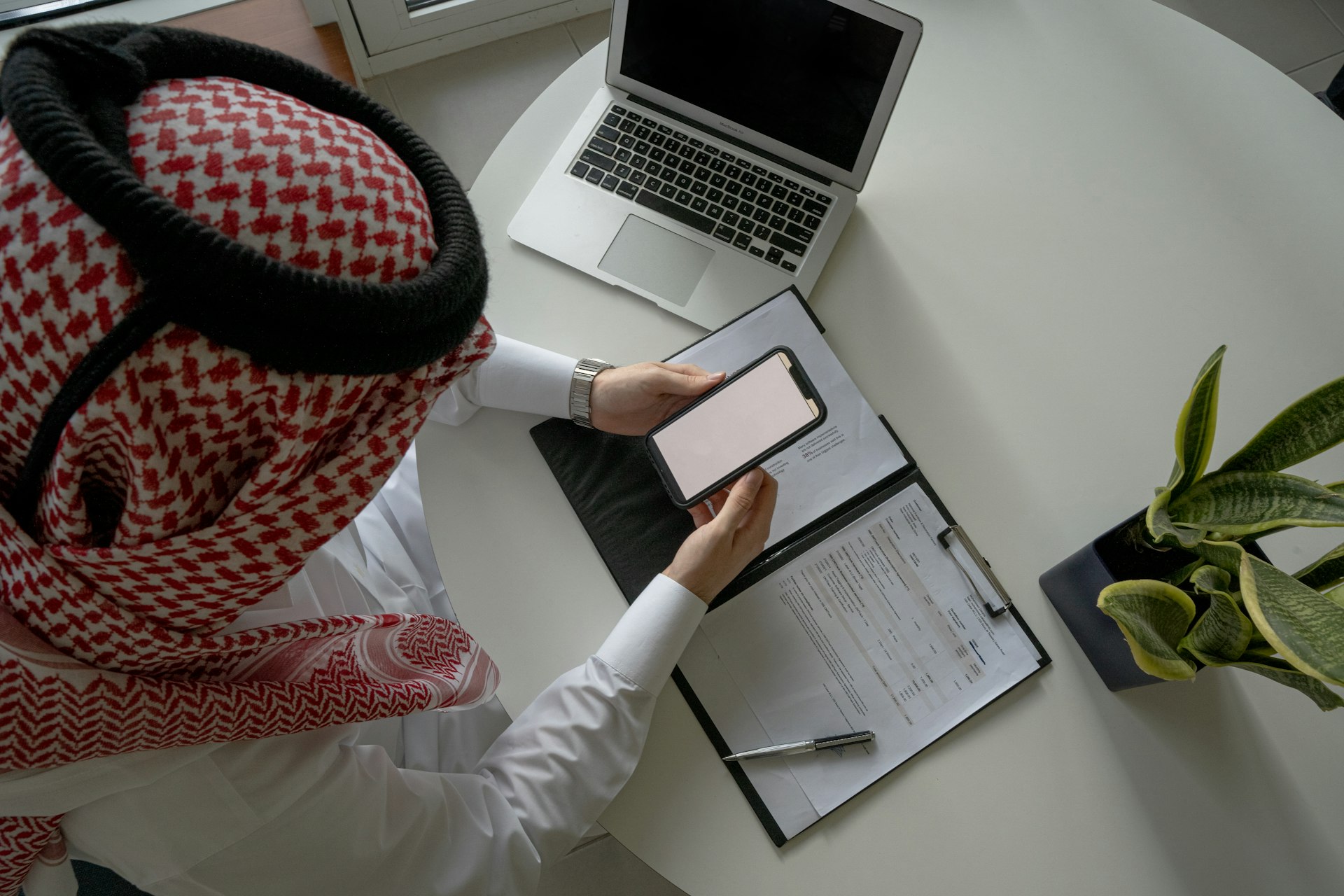 a person sitting at a desk with a laptop and a clipboard